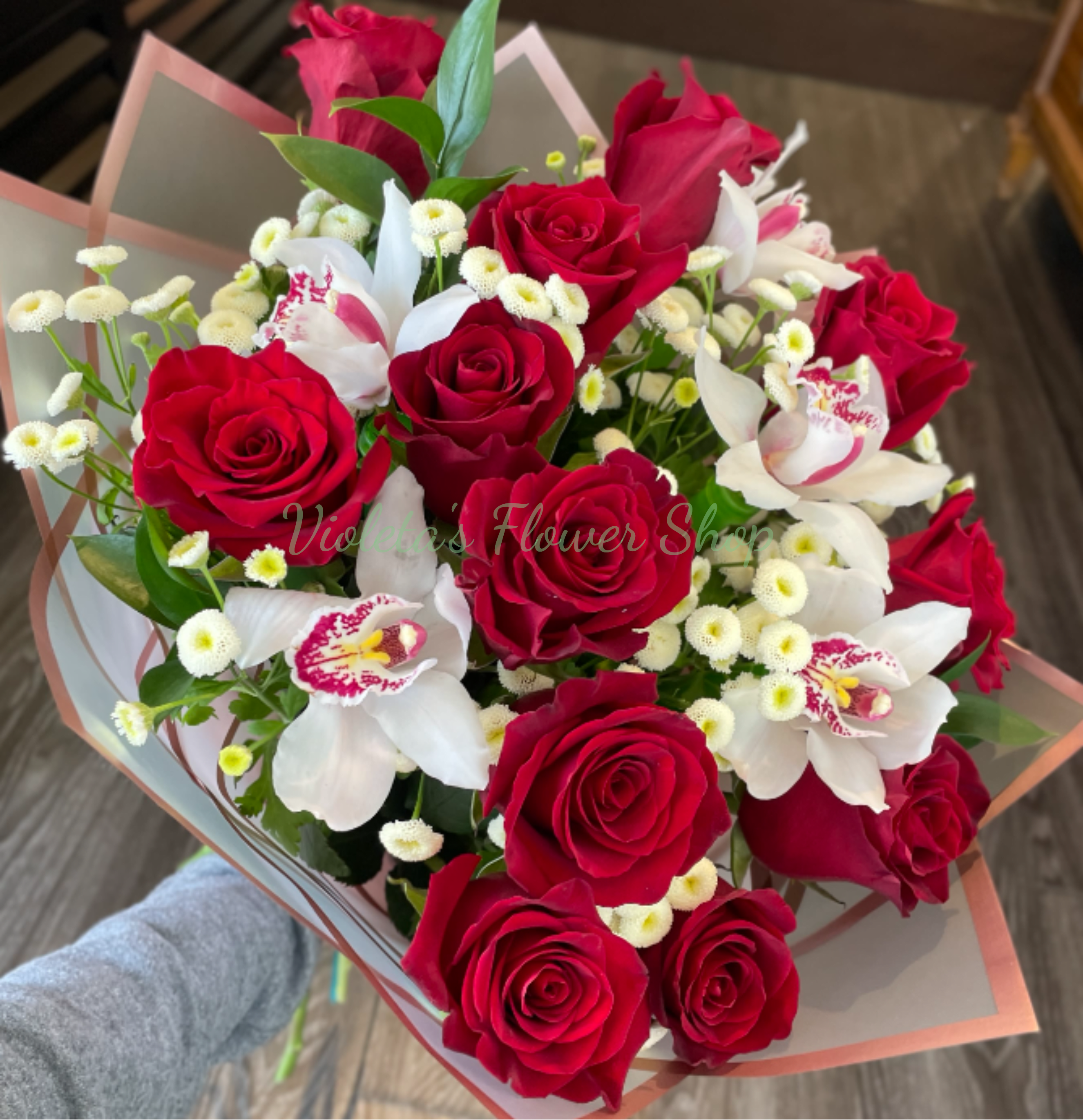 Roses and Orchids Hand Tied Bouquet - Vivid red roses paired with delicate white orchids create a romantic hand-tied bouquet perfect for anniversaries, Valentine's Day, or any special celebration where you want your person to feel deeply cherished. The strong red-and-white contrast reads classic and passionate, while the translucent pink-toned wrap lends a soft, feminine edge that makes the arrangement feel both festive and intimate.  