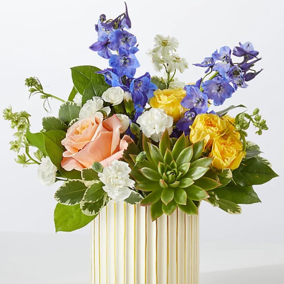 Bouquet of blue and yellow flowers with a peach rose in a striped vase