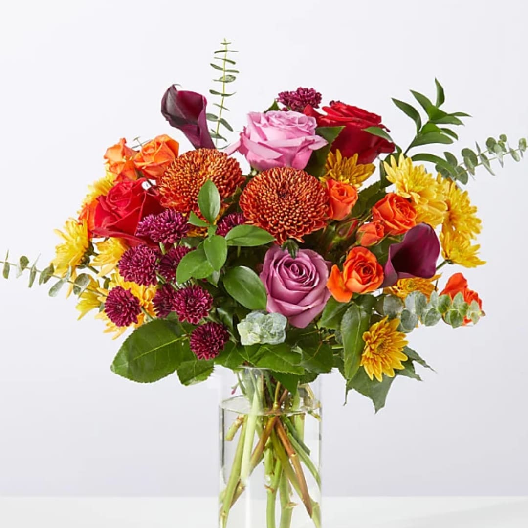 Mixed bouquet of roses, chrysanthemums, and calla lilies in a clear glass vase