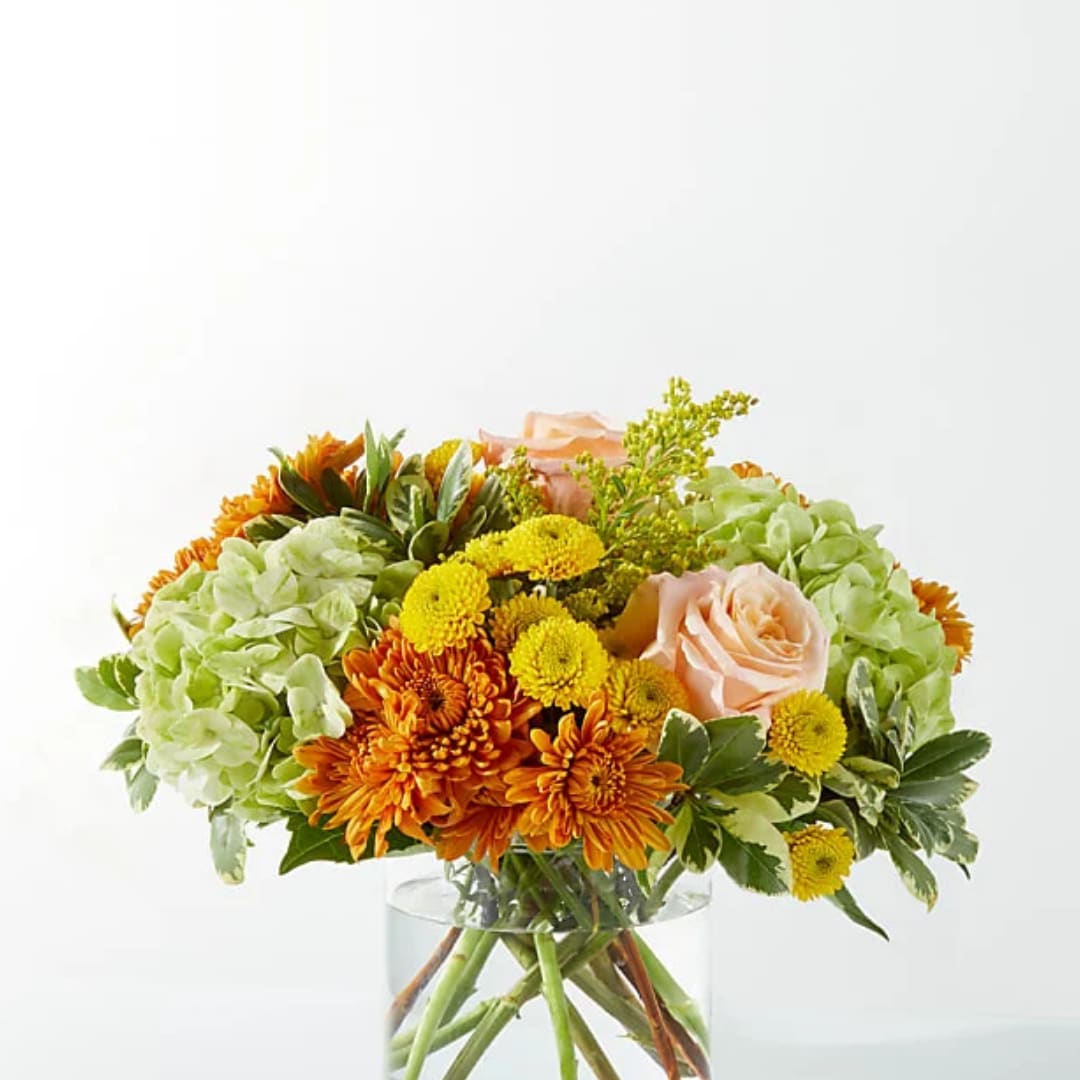 Orange and yellow flowers with pale pink roses in a clear glass vase