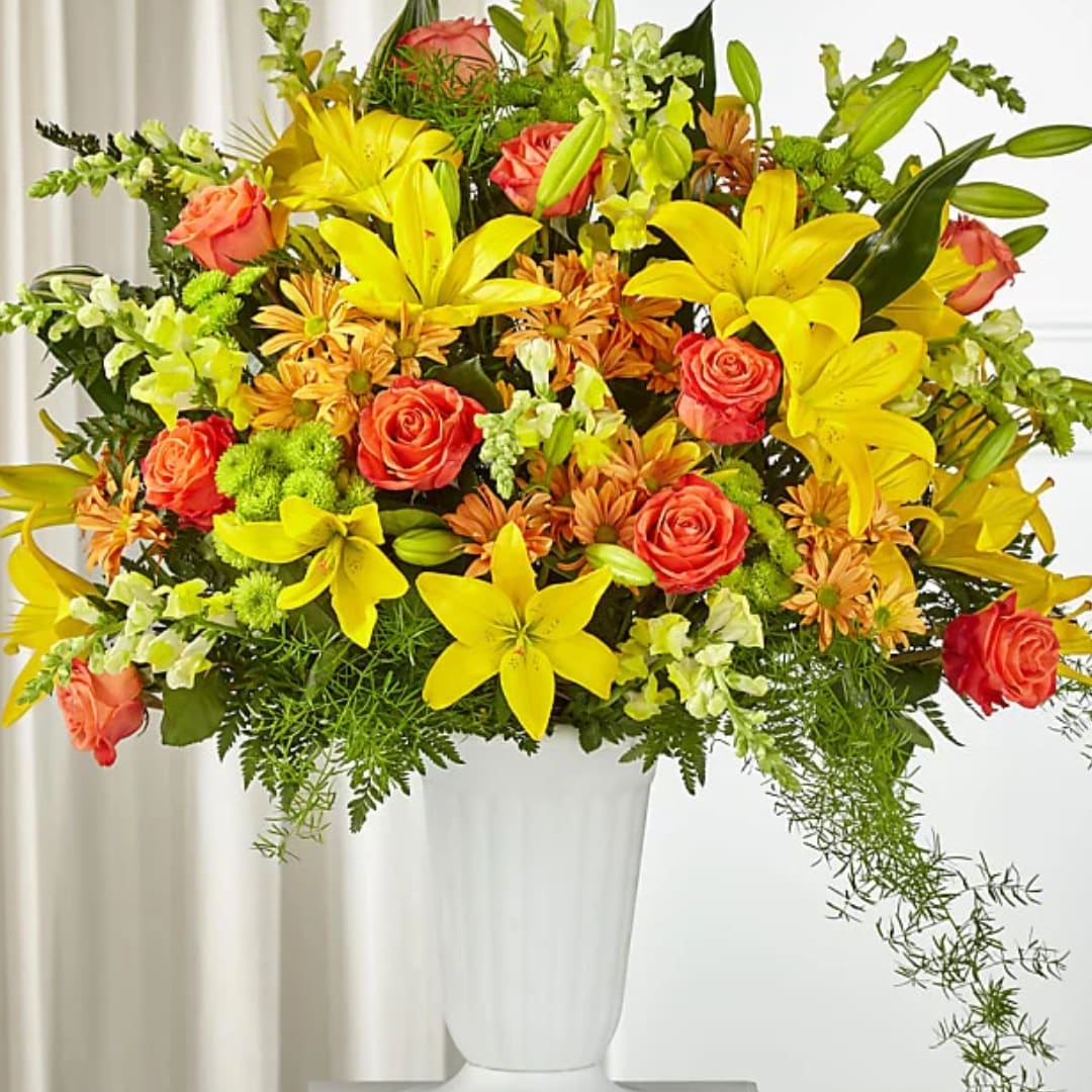 Bright mixed bouquet of yellow lilies, orange roses, and daisies in a white vase