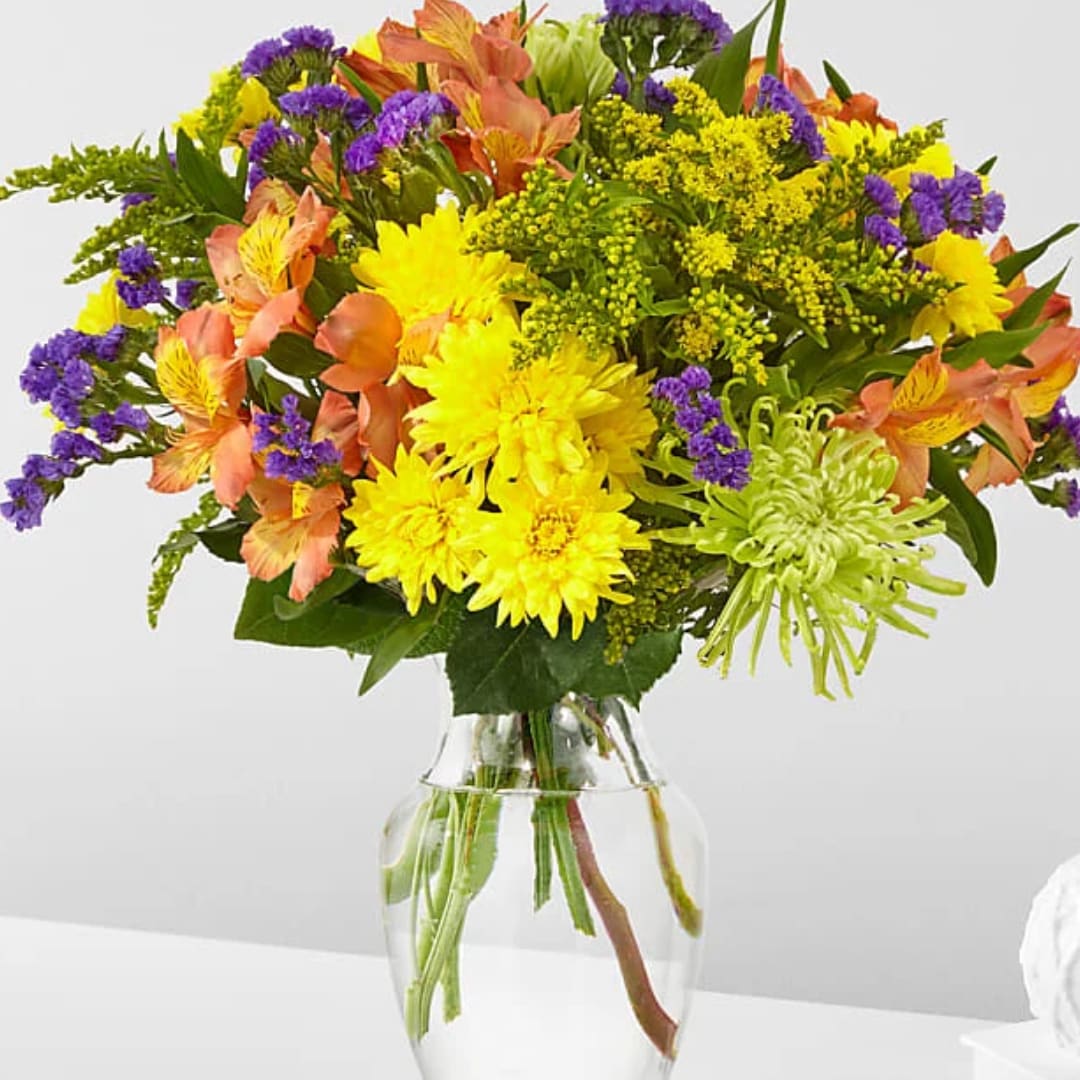 Mixed bouquet of yellow, purple, and peach flowers in a clear glass vase