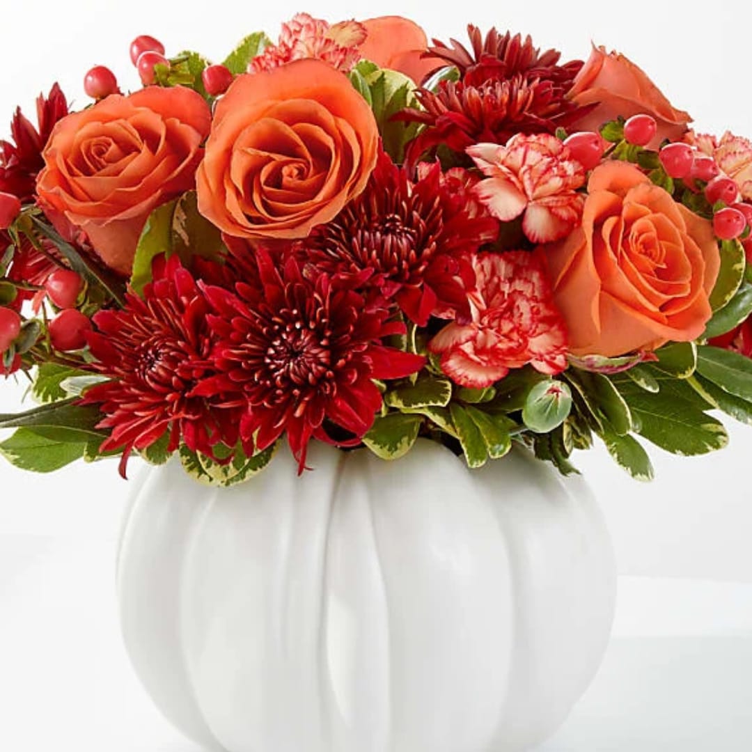 Orange roses and red chrysanthemums in a white pumpkin vase