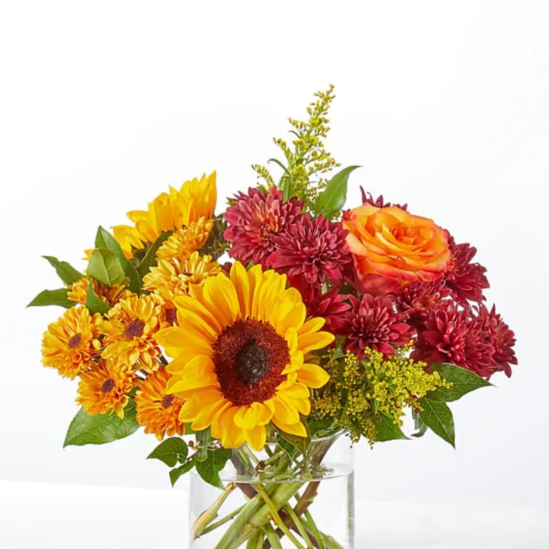 Bouquet of yellow sunflowers, orange roses, and burgundy chrysanthemums in a clear vase