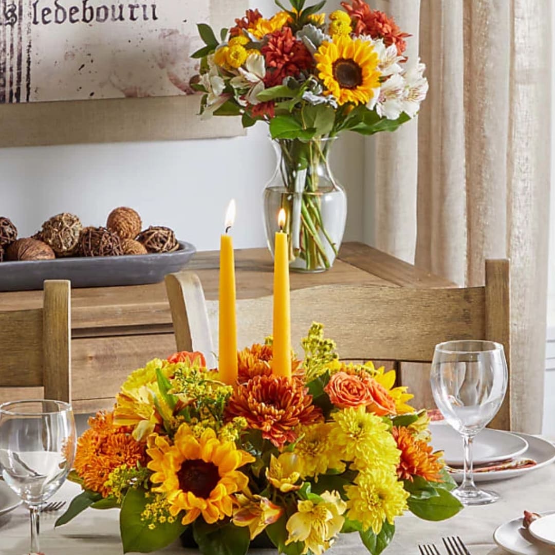 Yellow and orange floral centerpiece with two candles on a dining table