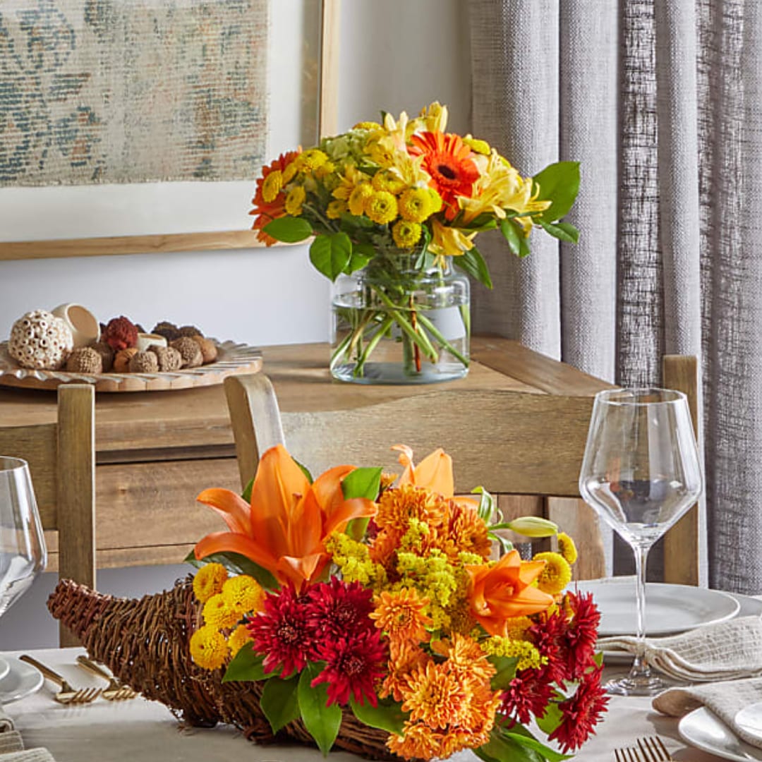 Two autumn flower arrangements with orange lilies and chrysanthemums, one in a glass vase and one in a wicker basket