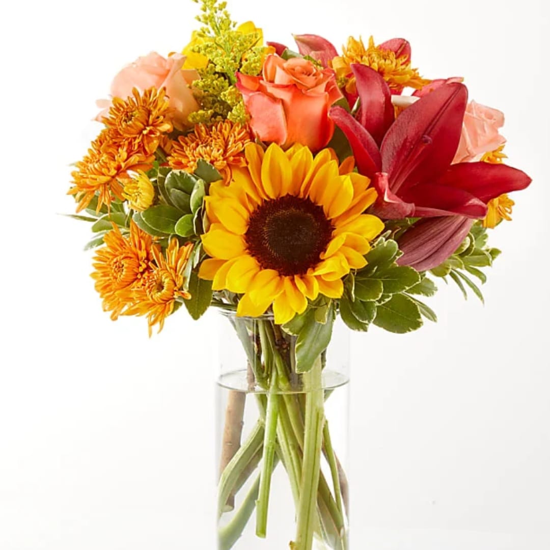 Bouquet of sunflowers, roses, and orange mums in a clear glass vase