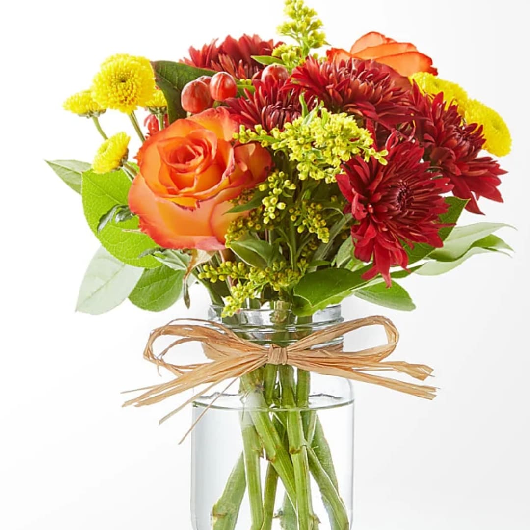 Orange roses and red chrysanthemums in a clear glass vase with a raffia bow