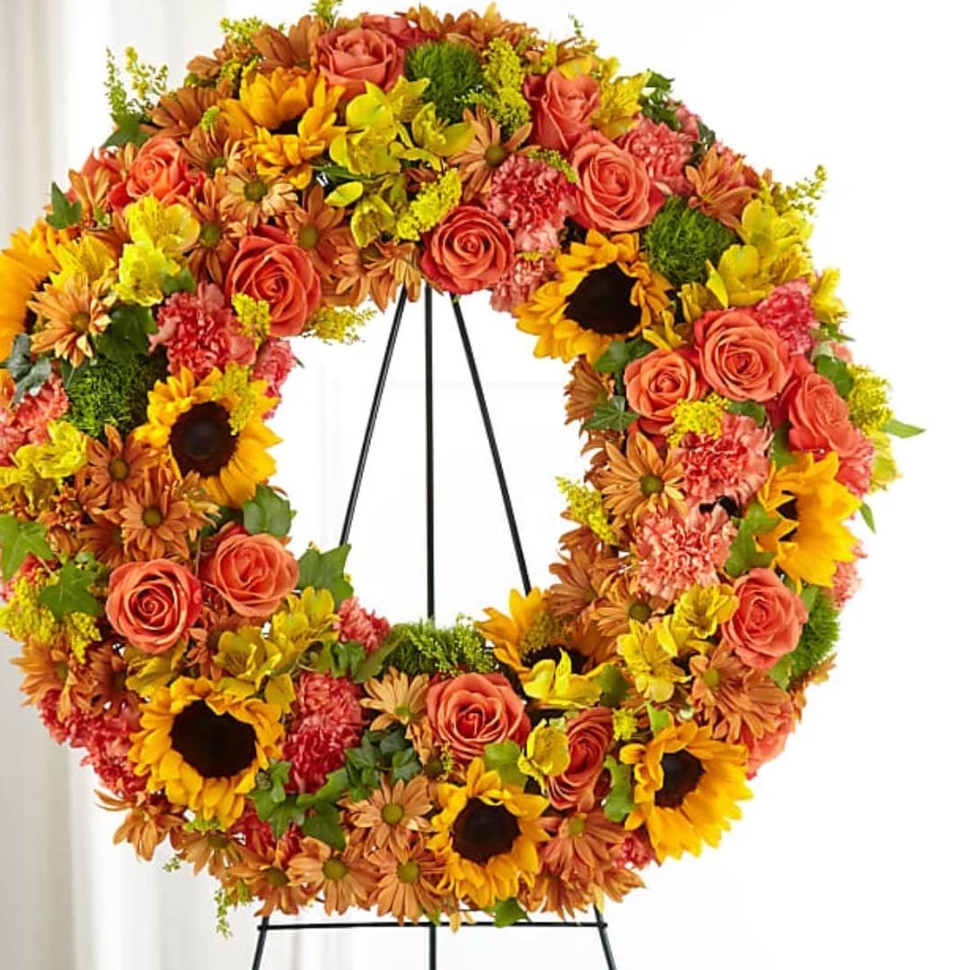 Colorful floral wreath on a black stand with roses, sunflowers, and carnations