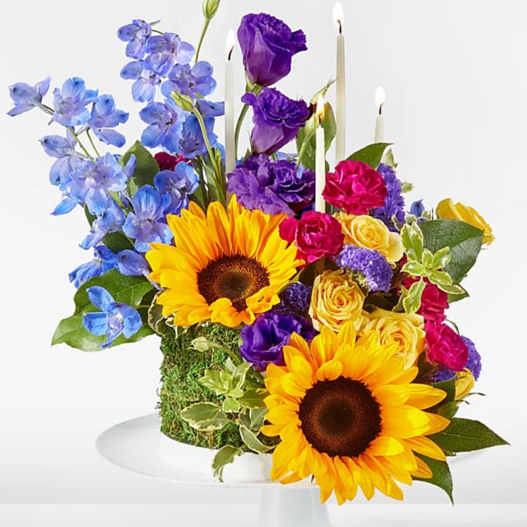 Colorful floral arrangement with sunflowers, roses, and tall candles
