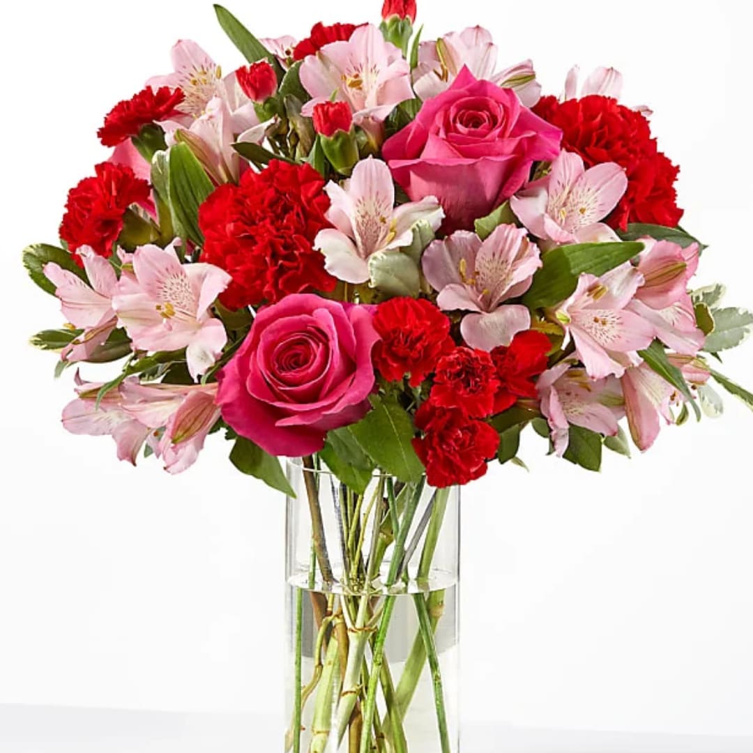 Pink roses, red carnations, and pale pink alstroemeria in a clear glass vase