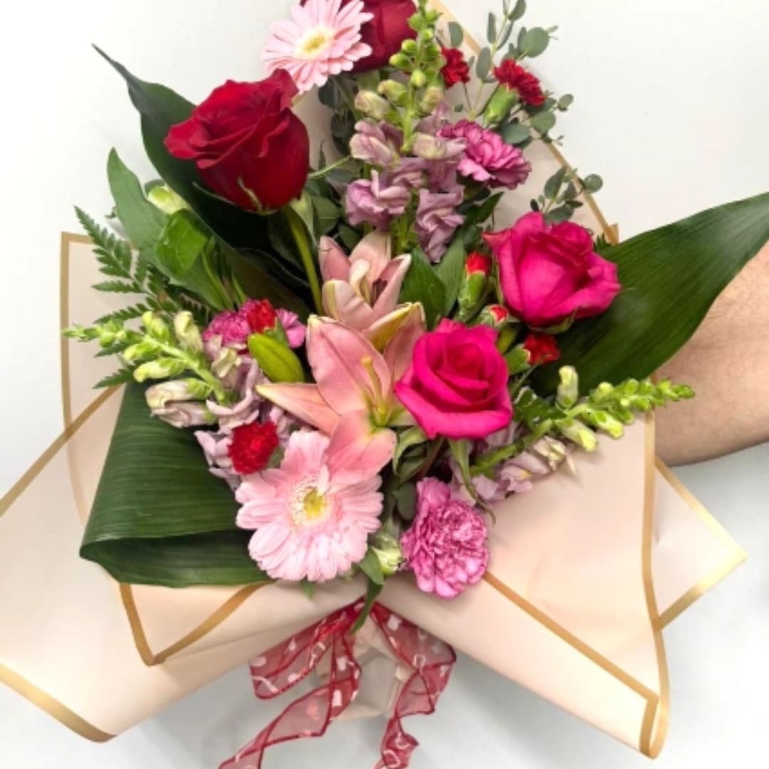 Bouquet of pink and red flowers wrapped in cream paper with a ribbon