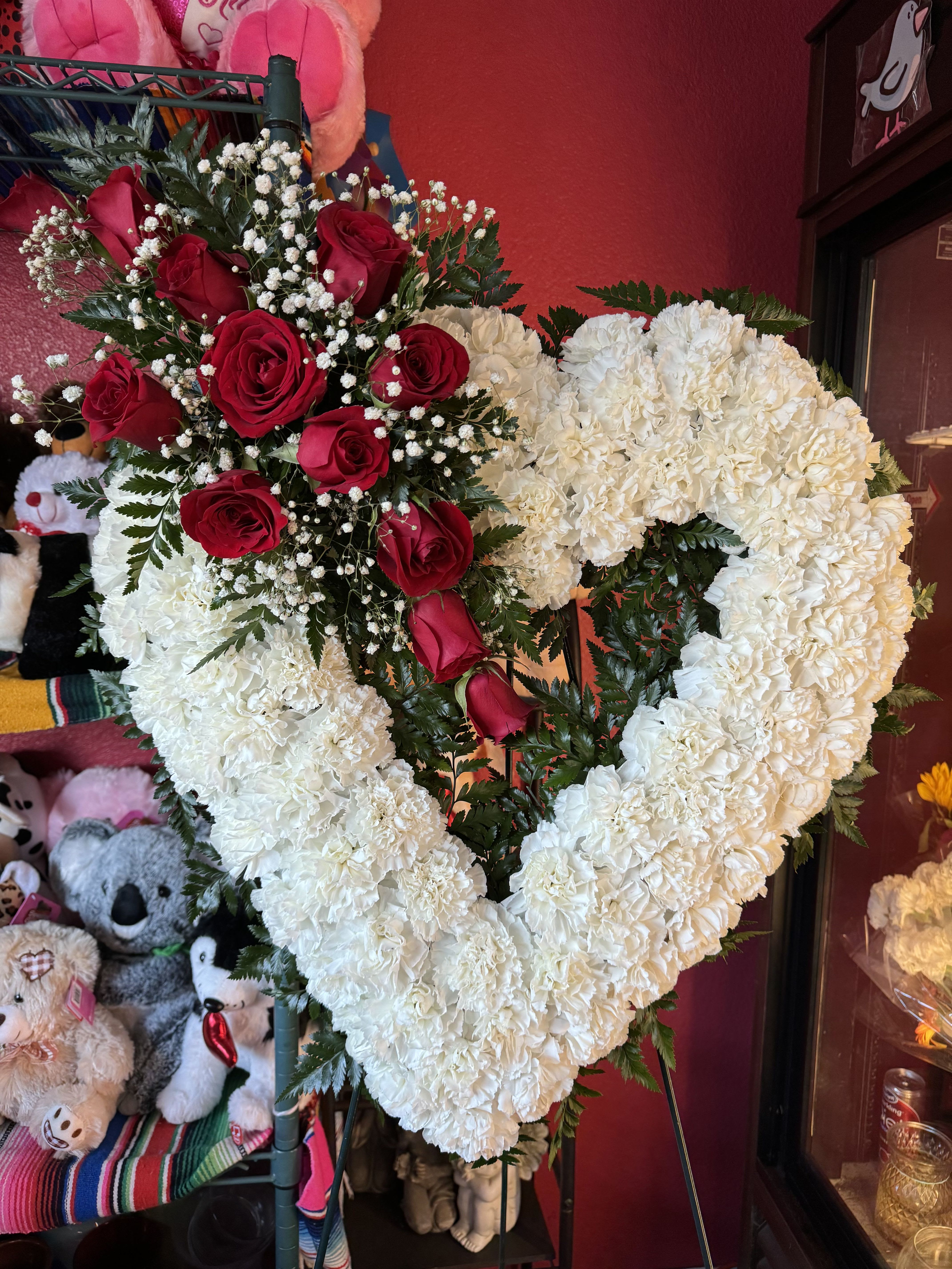 Everlasting Love Heart - A classic sympathy Heart featuring fresh carnations accented with a beautiful cluster of roses at the upper left, creating a graceful and heartfelt tribute.  If you would like one of the available colors below, please specify your preference in the Special Instructions section when placing your order, if not then the order will be made with red roses. Color requests are subject to availability.  Available Colors:  1)Pink 2)Yellow 3)Off-White 4)Fuchsia 