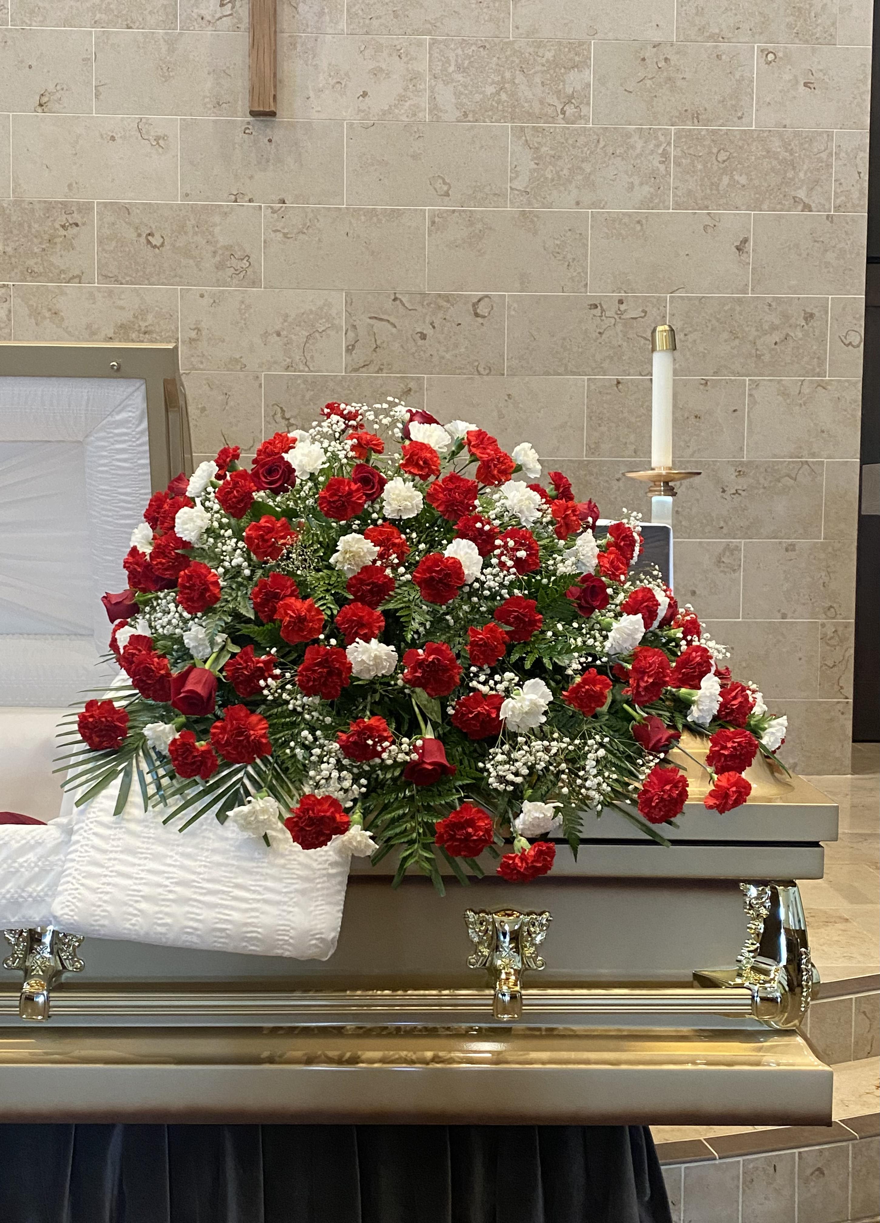 Sympathy Casket Spray - A classic sympathy casket spray featuring fresh carnations accented with greenery.  If you would like one of the available colors below for the roses only, please specify your preference in the Special Instructions section when placing your order, if not then the order will be made with red roses. Color requests are subject to availability.  Available Colors:  1)Pink 2)Yellow 3)Off-White 4)Fuchsia
