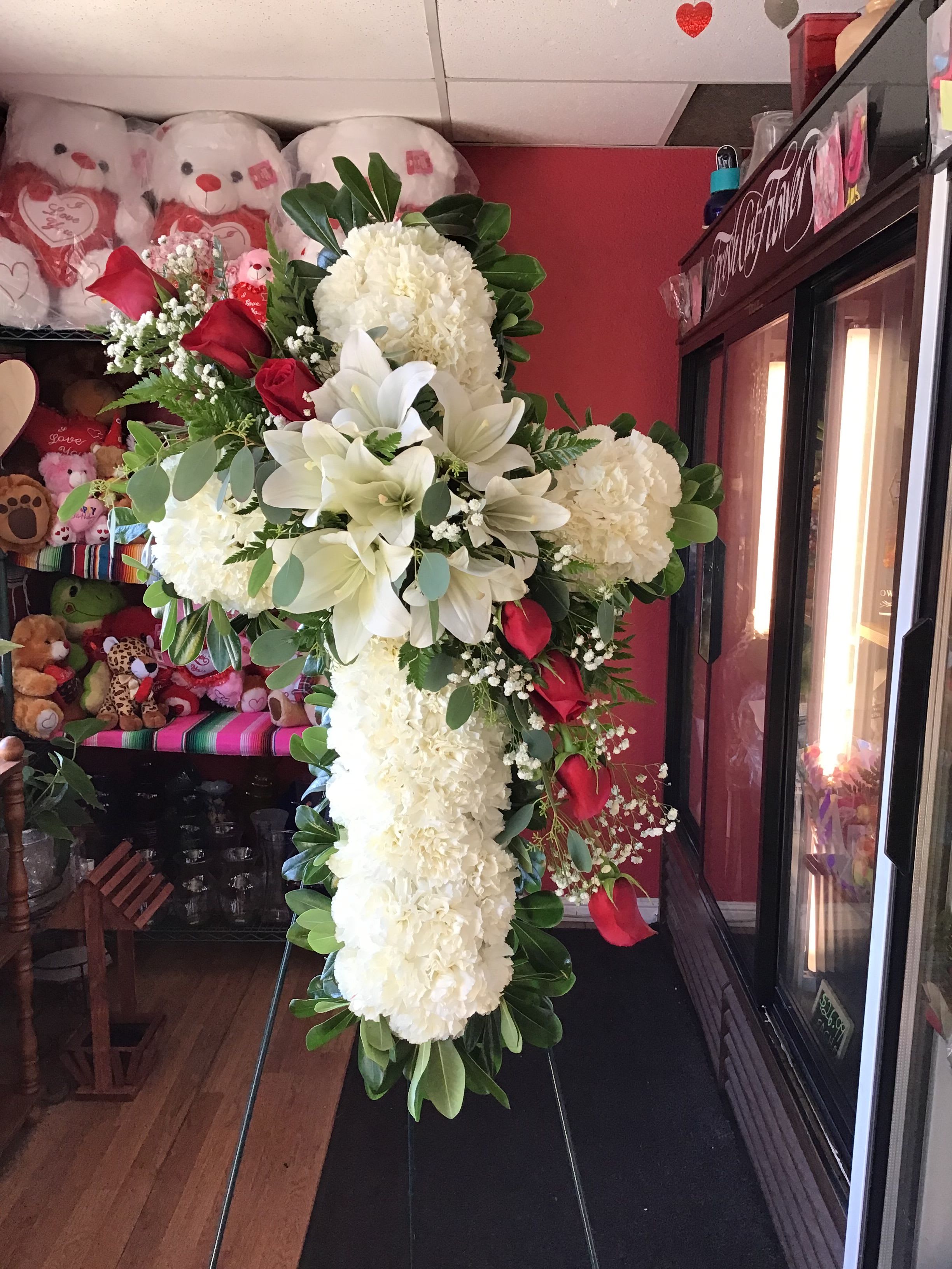 Faith and Love - Beautiful cross made with carnations, roses, and lilies accompanied by greenery.   If you would like one of the available colors below, please specify your preference in the Special Instructions section when placing your order, if not then the order will be made with red roses. Color requests are subject to availability.  Available Colors:  1)Pink 2)Yellow 3)Off-White 4)Fuchsia