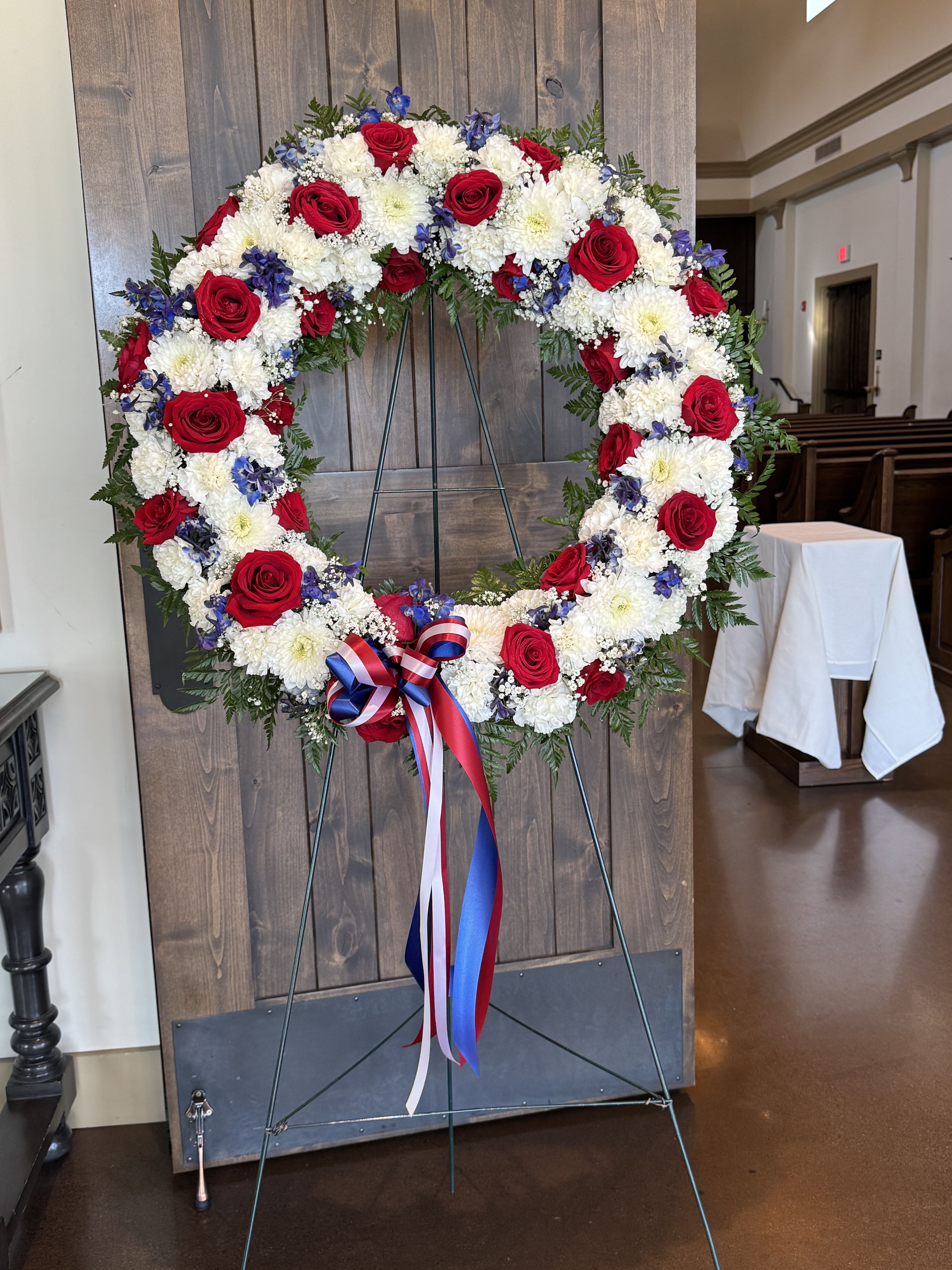 red, white, and blue Sympathy Wreath  - Wreath made of roses, delphiniums, chrysanthemum, carnations, and greenery.   Perfect arrangement for Memorial Day, Veterans Day or any other similar occasion.