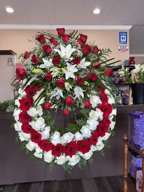 Sympathy Rose Wreath  - This beautiful wreath comes with exclusively with Roses and Lilies. This standing wreath symbolizes everlasting love and the memories that remain forever in our hearts. Displayed on a wire easel, it offers a meaningful expression of sympathy and support during a time of loss.