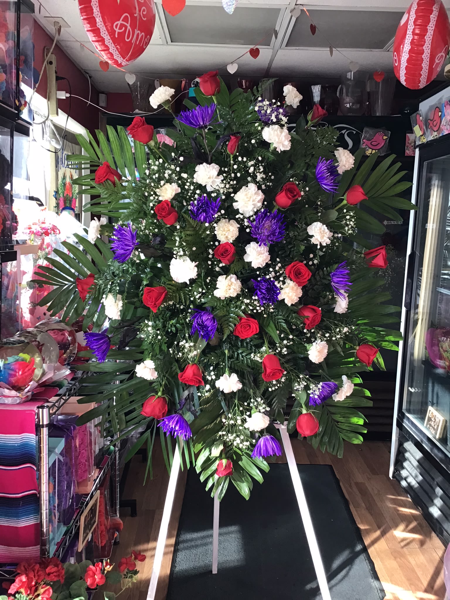Purple Rain  - The Purple Rain Standing Spray is a beautiful expression of love, remembrance, and heartfelt sympathy. Designed with rich purple and classic red accents against fresh white blooms and lush greenery, this elegant standing tribute symbolizes admiration, dignity, and everlasting memories. Displayed on a standing easel, it offers comfort and support to family and friends while honoring the life of a loved one with grace and beauty.