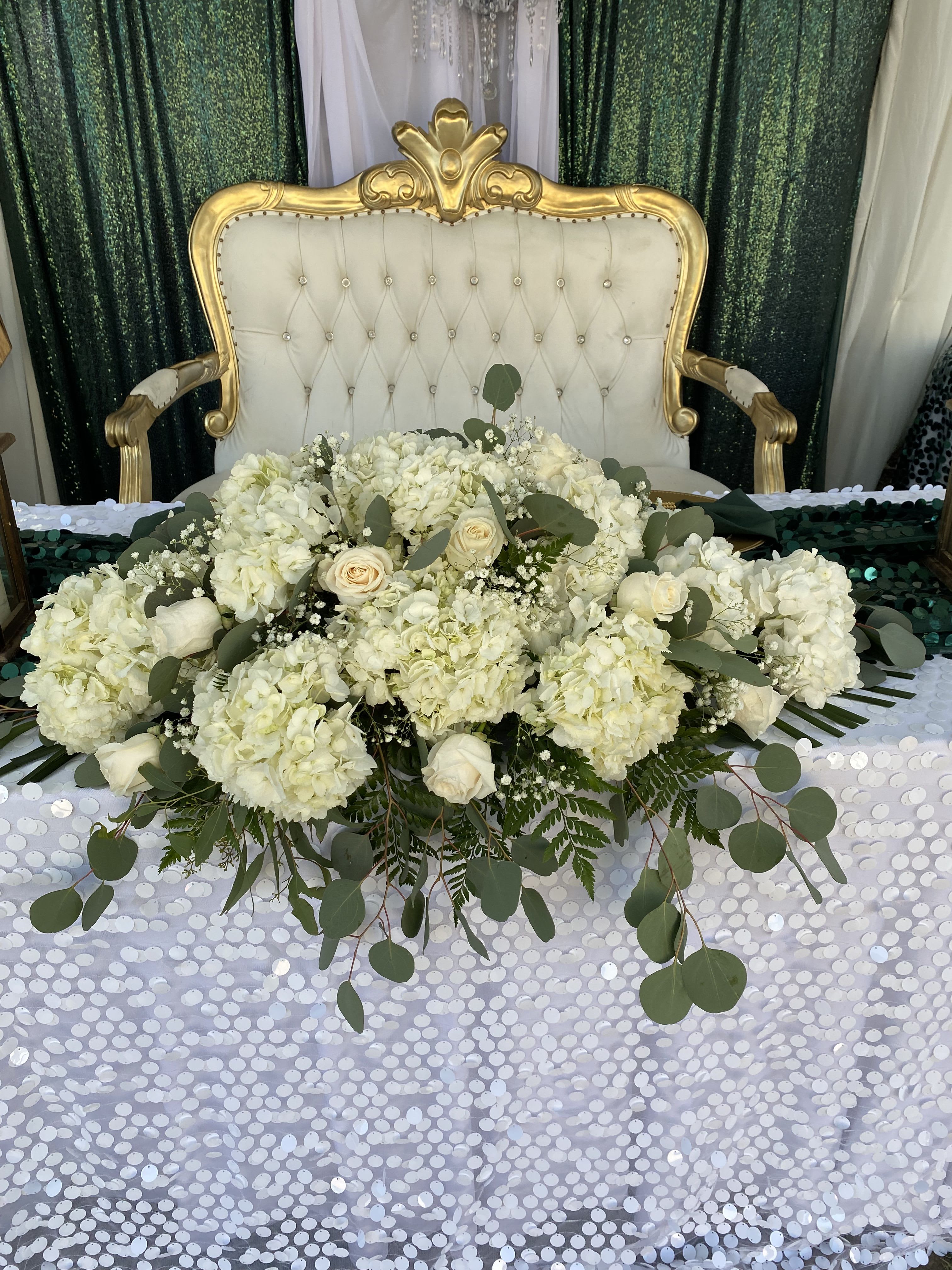 Everlasting Elegance Centerpiece - Designed to bring refined beauty to life's most meaningful moments, the Everlasting Elegance Centerpiece features a graceful blend of soft white blooms accented with lush greenery. Its elongated design makes it an eye-catching focal point for sweetheart tables, altar displays, memorial services, or elegant receptions. 