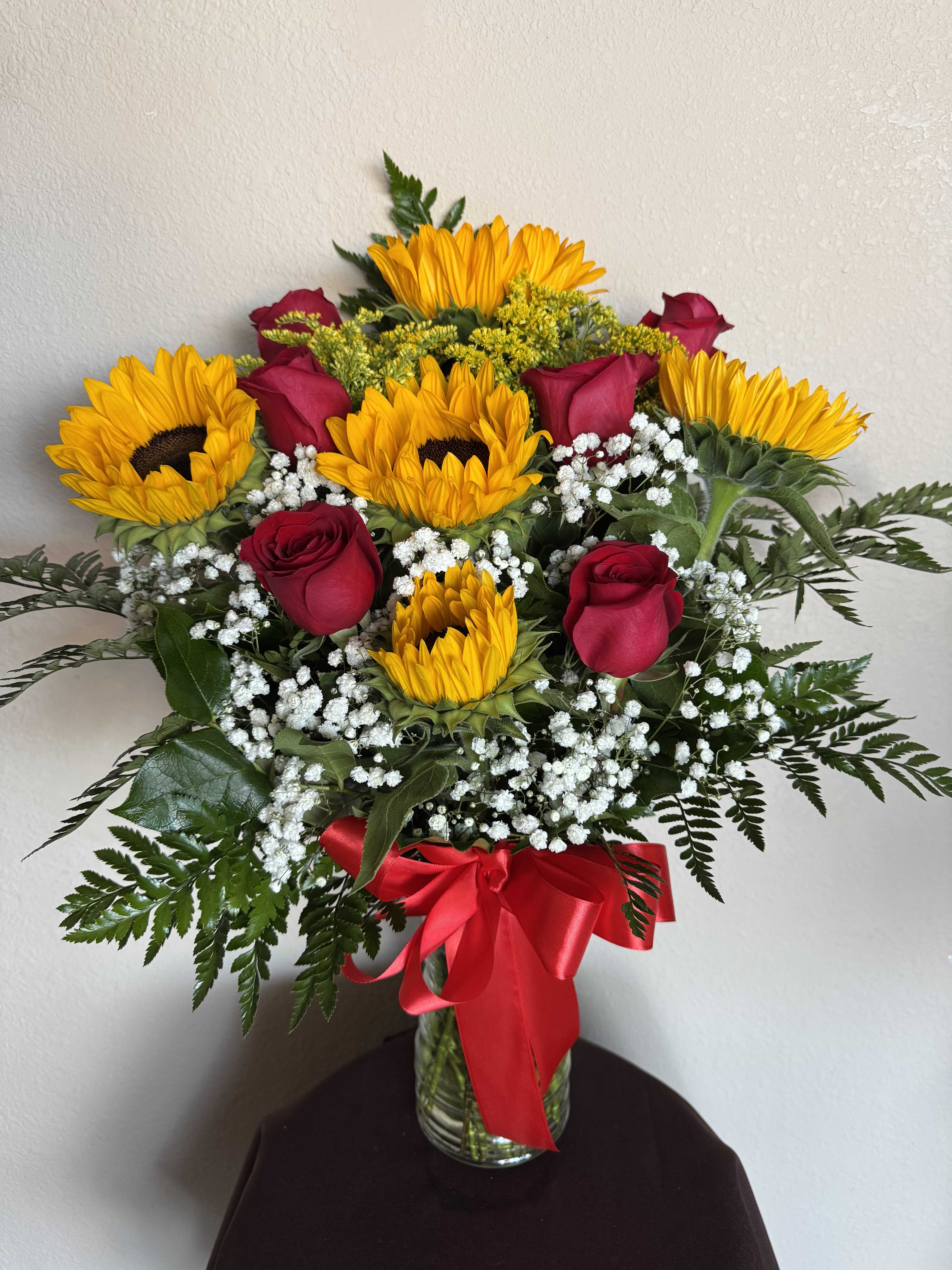 Sunflowers and red roses in a glass vase with a red ribbon