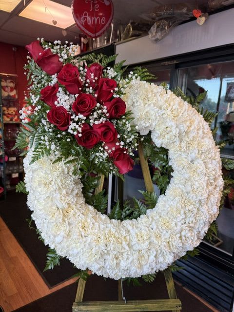 Heart-shaped floral wreath with red roses and white flowers on an easel