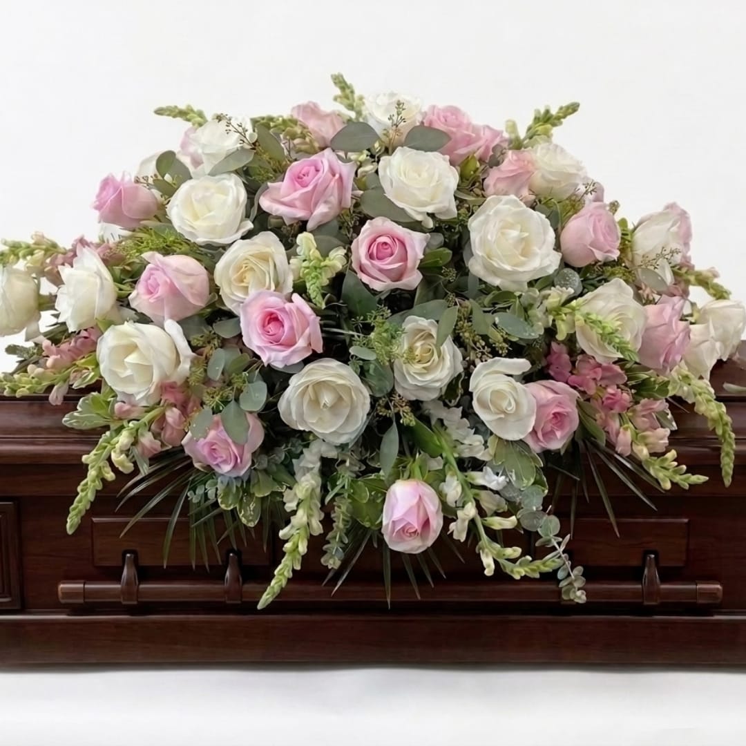 Pink and white rose arrangement on a dark wooden casket