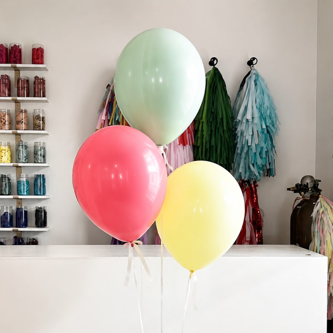 Three pastel balloons in a shop interior, with ribbon tails.