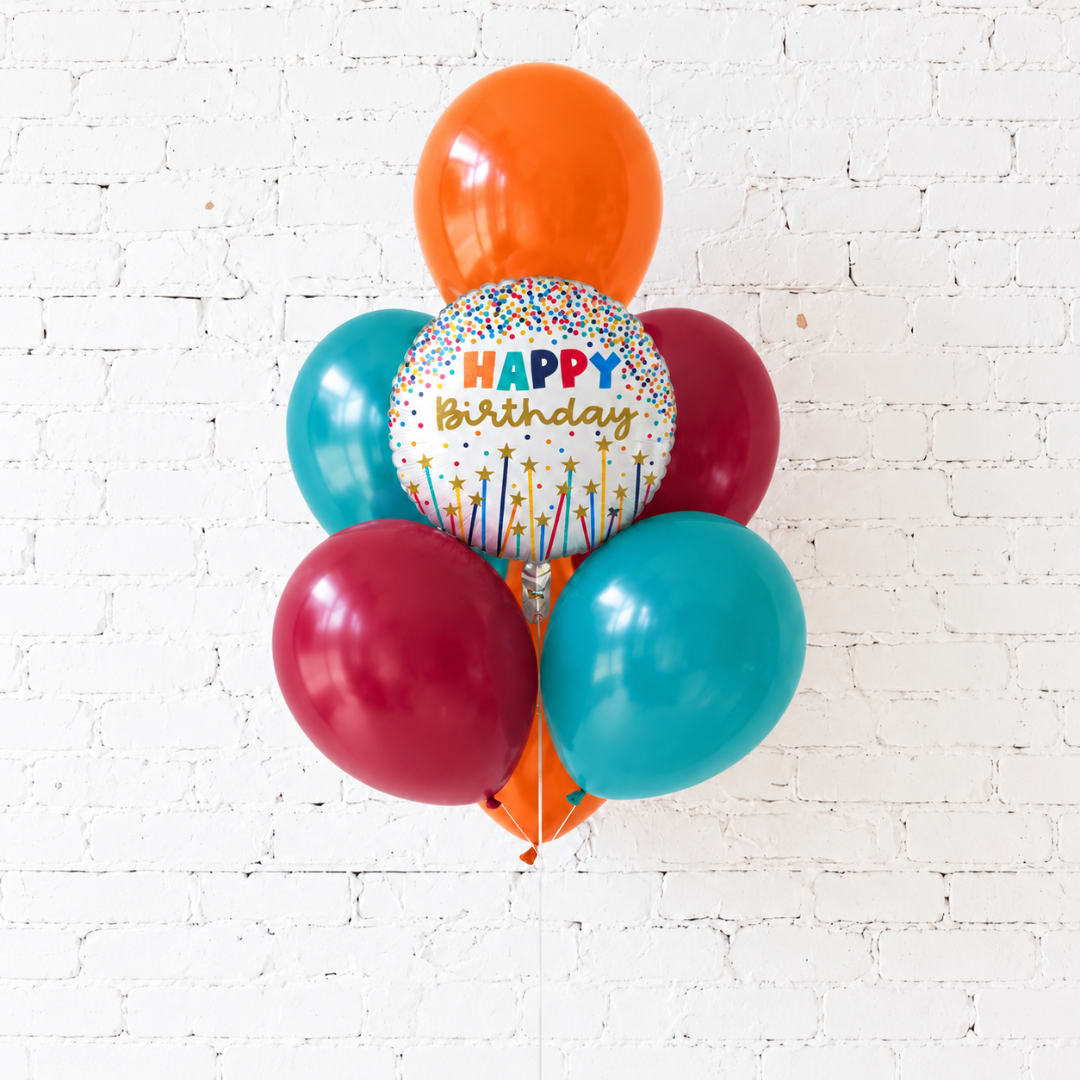 Cluster of birthday balloons against a white brick wall
