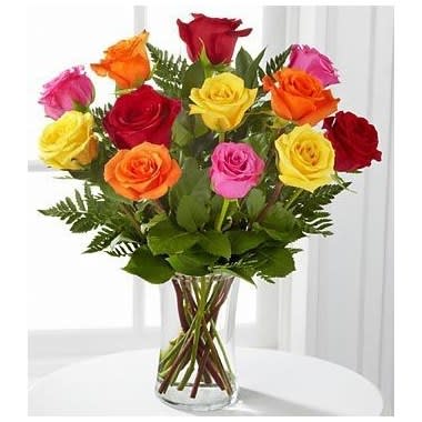 Arrangement of mixed-color roses in a clear glass vase on a white table.