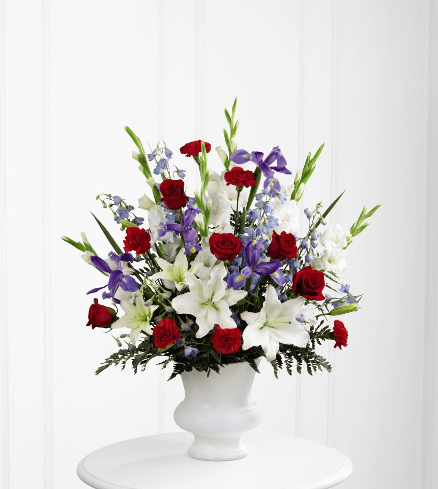 Tall red, white, and blue arrangement with lilies, roses, carnations, and iris in a white urn