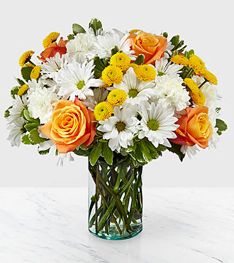 Mixed bouquet of orange roses, white daisies, and yellow poms in a clear glass cylinder vase
