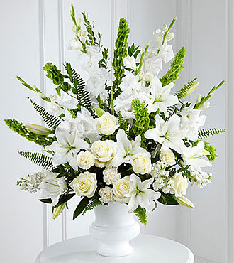 Large white arrangement of lilies, roses, and carnations in a white pedestal vase