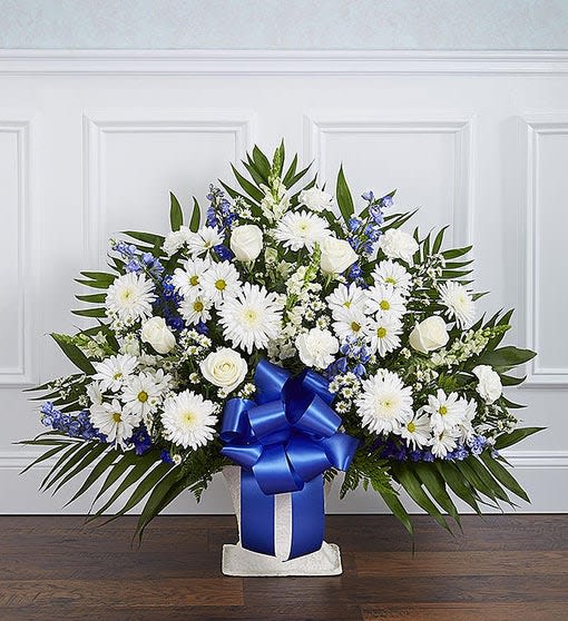 Tall white and blue floral arrangement with a large blue bow in a white container