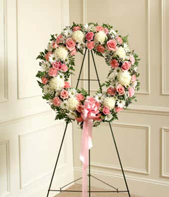 Standing wreath of pink roses and white flowers on an easel with a pink bow
