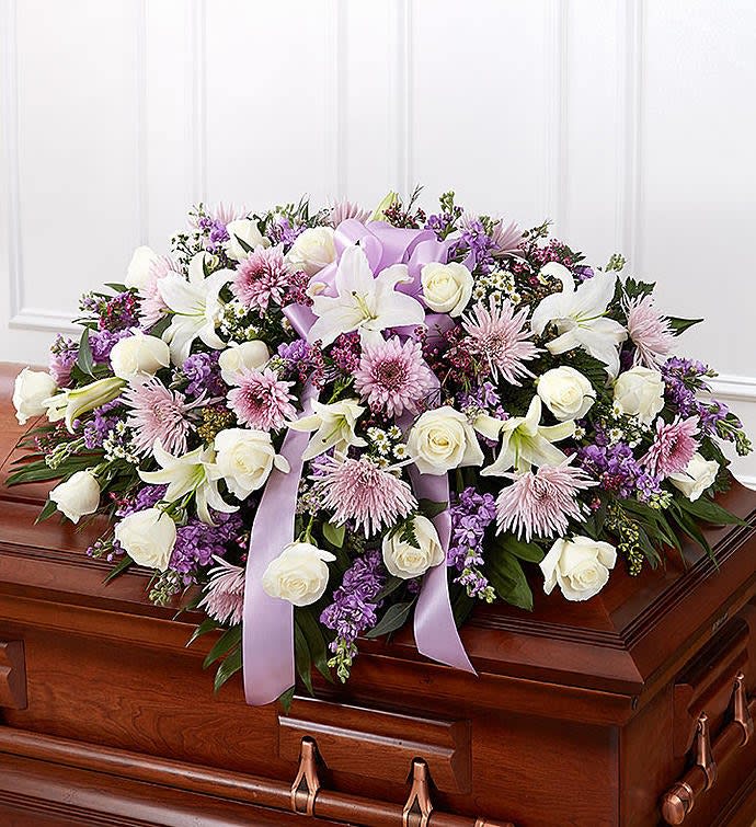 Lavender and white casket spray with roses, lilies, and mums on a wooden casket.