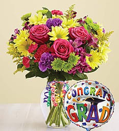 Bright mixed bouquet in a glass vase with a colorful Congrats Grad balloon