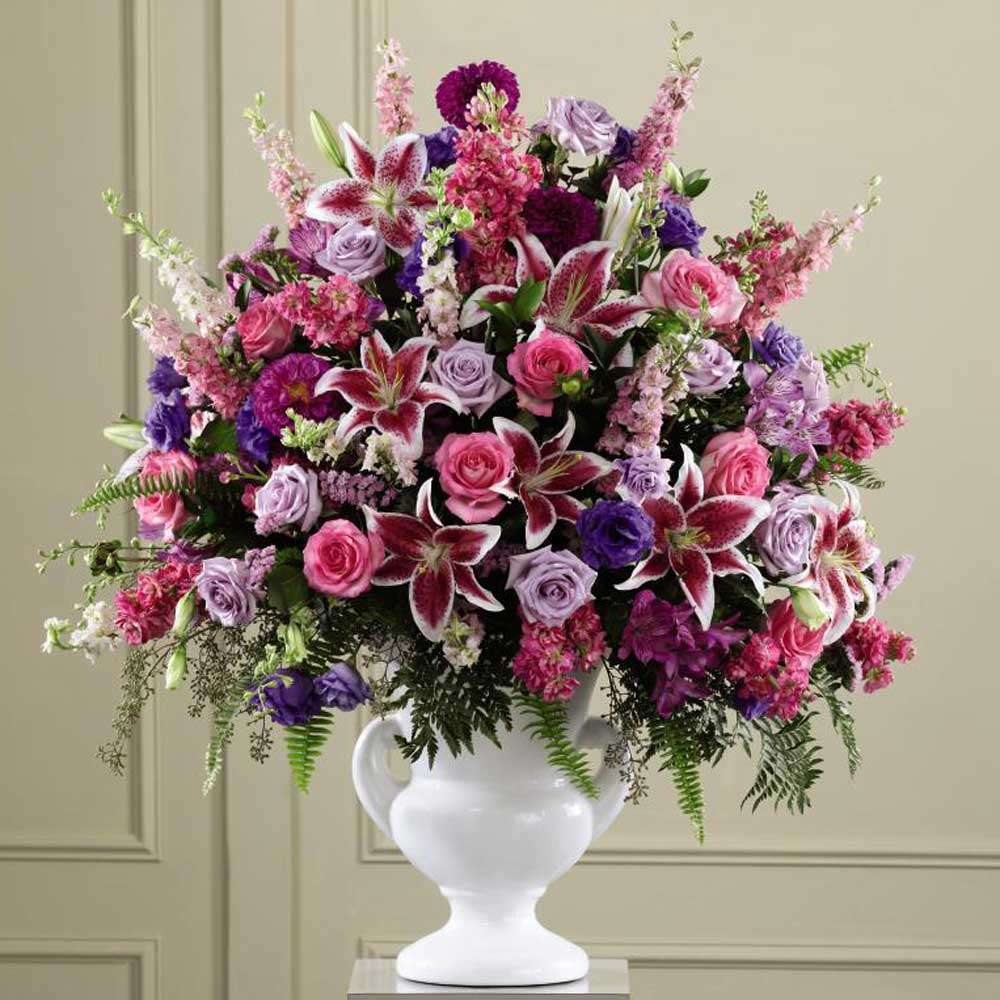 Large pink and purple flower arrangement with lilies and roses in a white urn vase