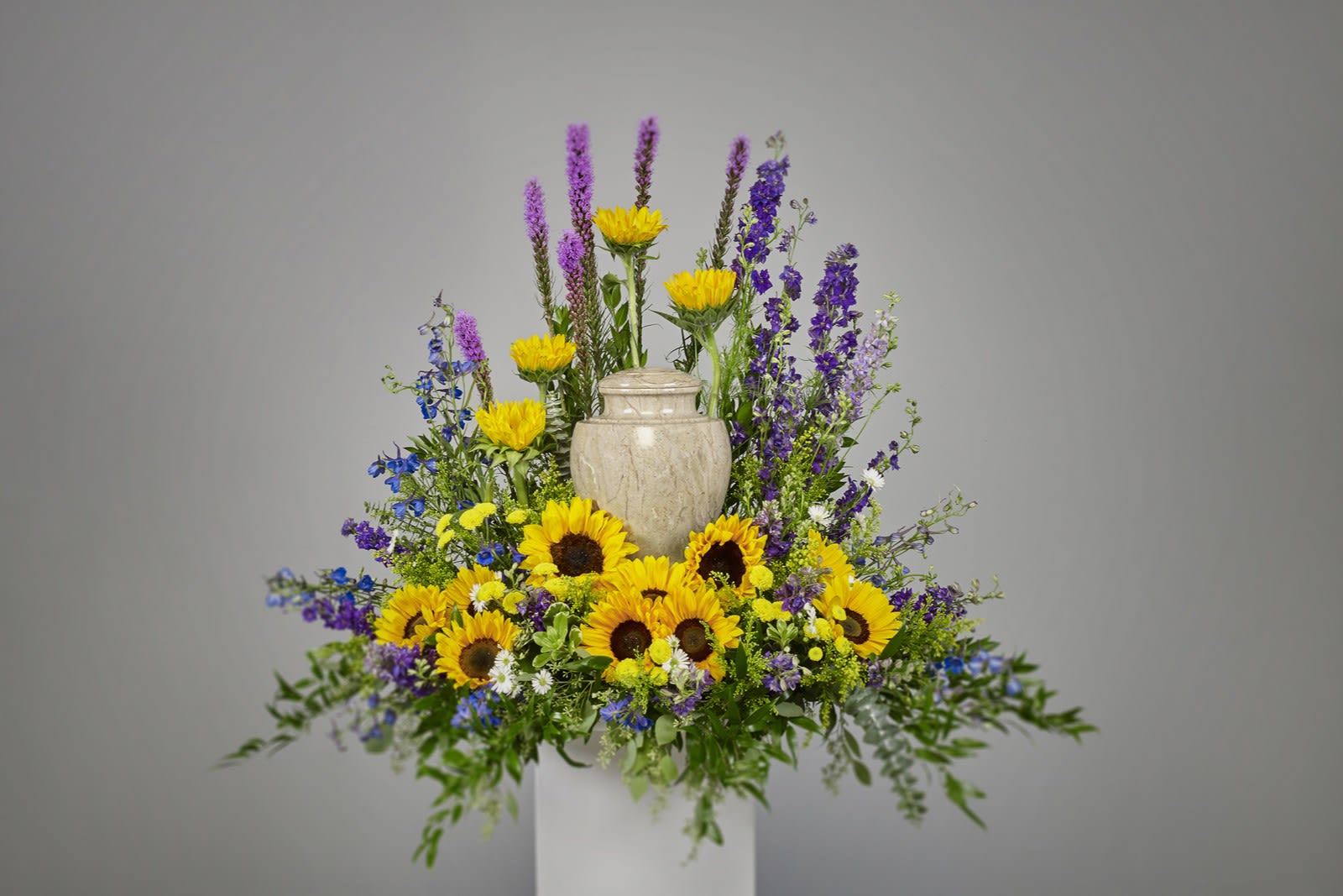 Cremation floral display with yellow sunflowers and purple blooms surrounding a stone urn