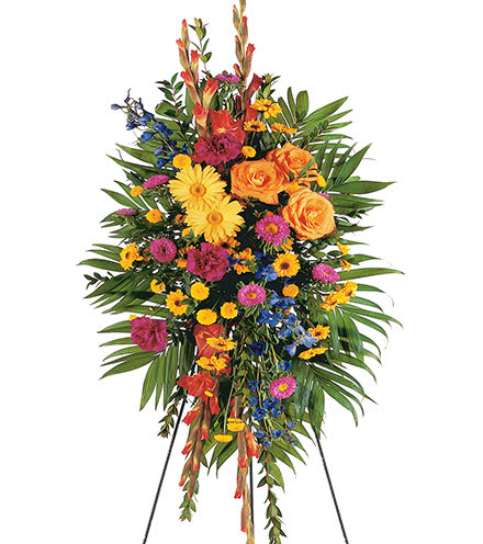 Tall standing spray of bright yellow, orange, pink, and blue flowers on an easel.