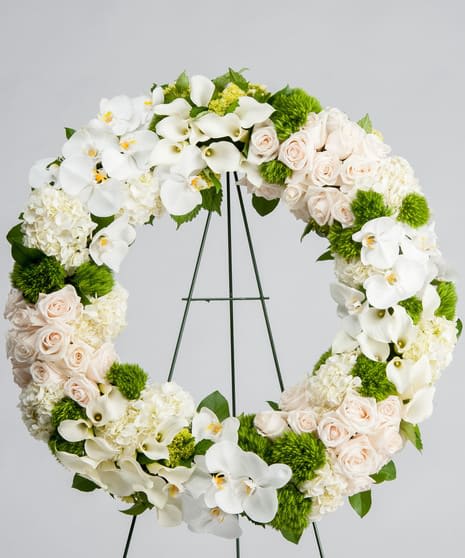 Large wreath of white orchids, calla lilies, hydrangeas and blush roses on a metal easel stand