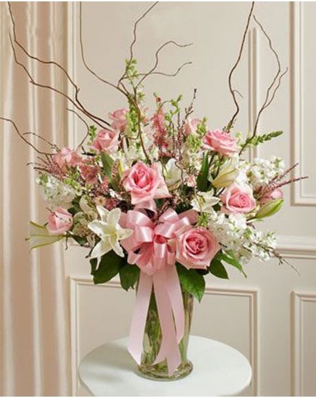 Tall pink and white arrangement with roses and lilies in a clear vase with a pink bow