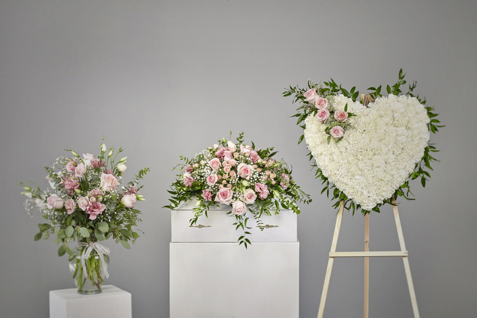 Sympathy set with pink and white arrangements and a white heart wreath on a stand