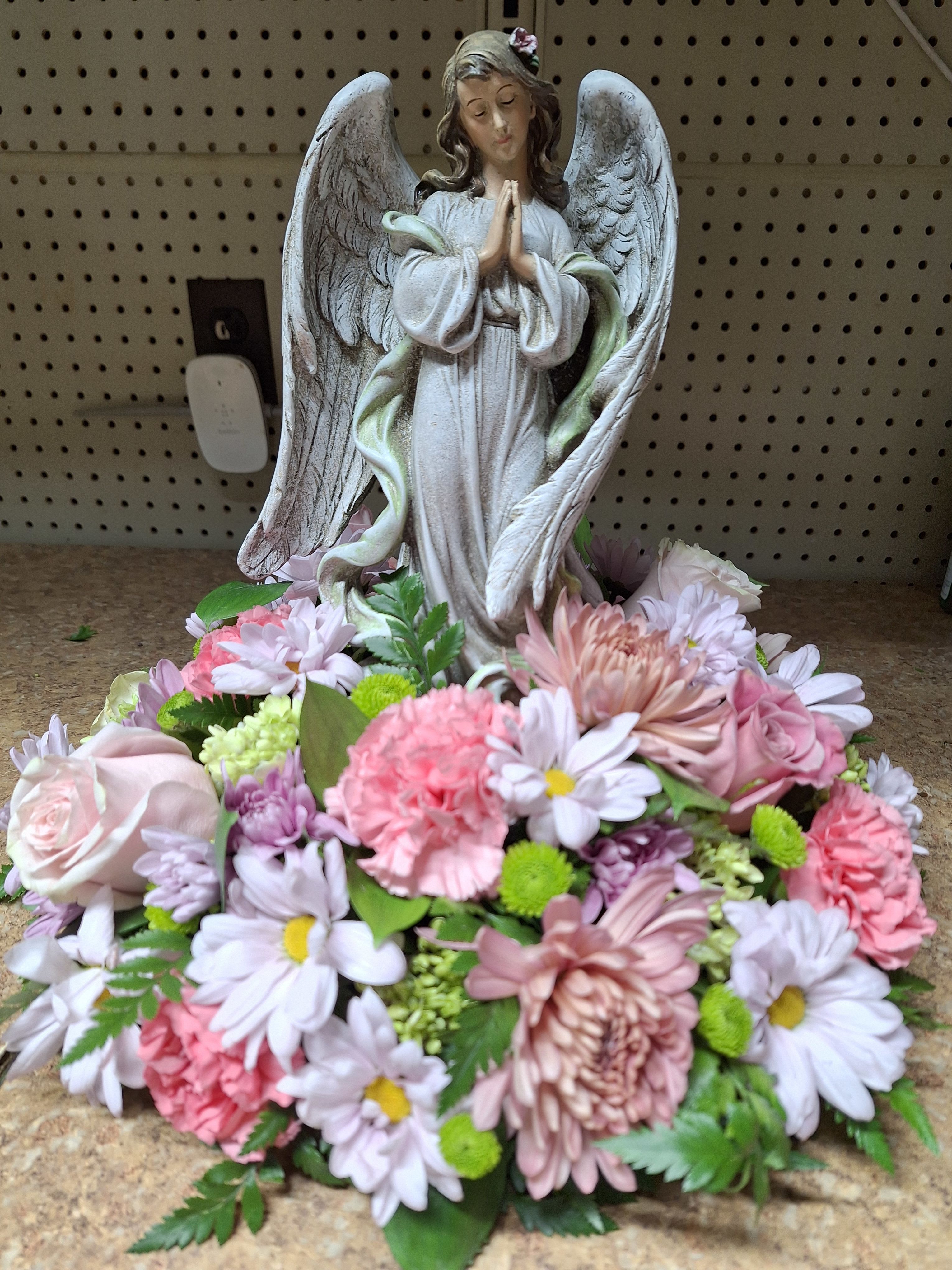 Angel figurine surrounded by a low mound of pink and white flowers.