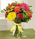 Mixed bouquet of bright flowers in a clear glass vase with a yellow ribbon