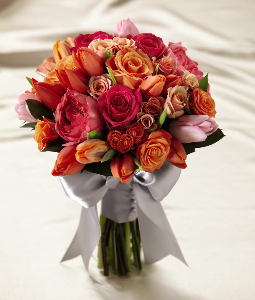 Hand-tied bouquet of orange, coral, and pink roses with tulips, wrapped in white satin ribbon and bow