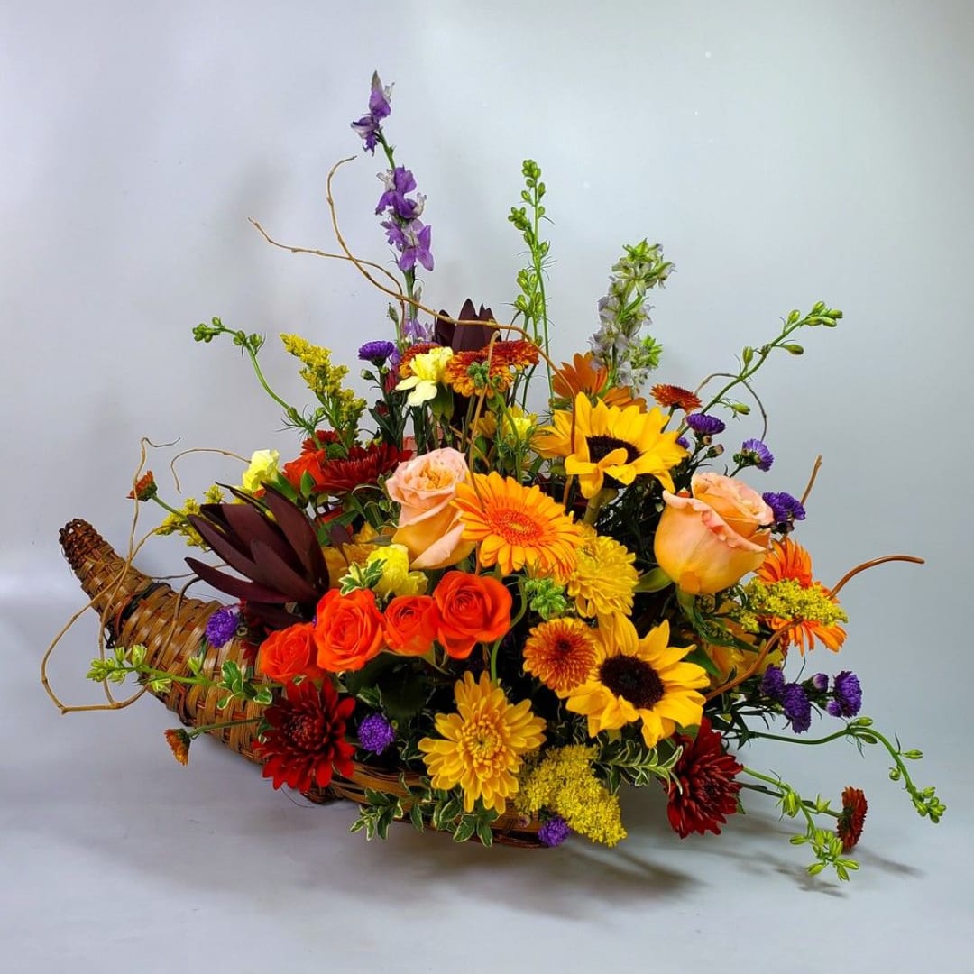 Mixed bouquet in a woven basket with sunflowers, roses, and chrysanthemums