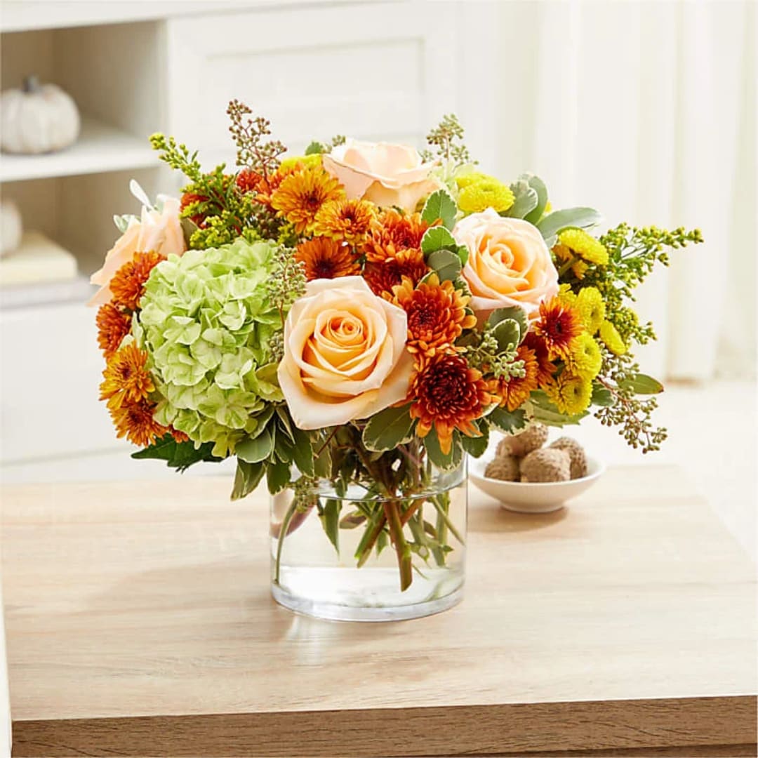 Peach roses and orange chrysanthemums in a clear glass vase