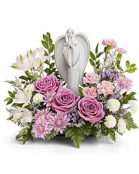 Pink roses and white lilies arranged around a white angel figurine