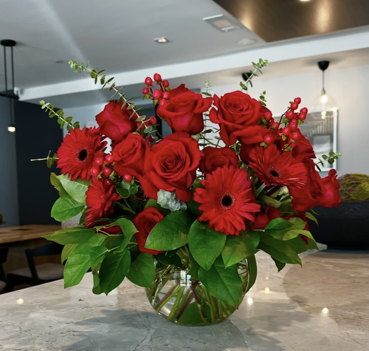 Lovely Gerberas - Red roses and gerbera daisies with green foliage and white accents in a clear glass vase-bold, romantic arrangement perfect for anniversaries or heartfelt occasions.