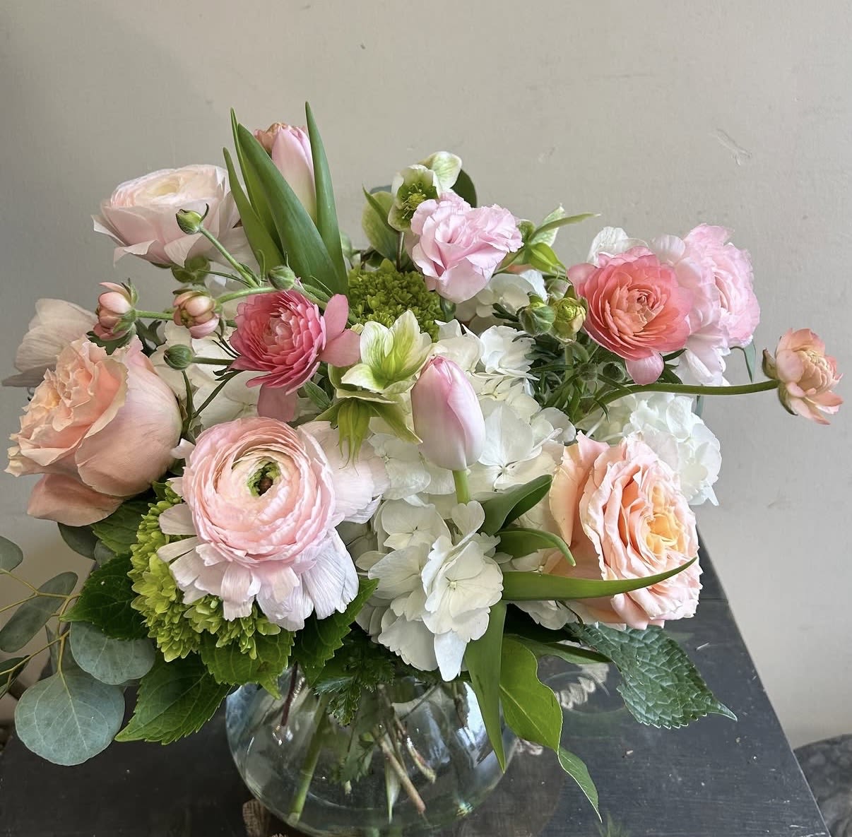 Spring Melody - Soft pink, white and peach roses, ranunculus, tulips and hydrangeas in a rounded garden-style bouquet with green accents, arranged in a clear glass vase - perfect for anniversaries or saying "thinking of you."